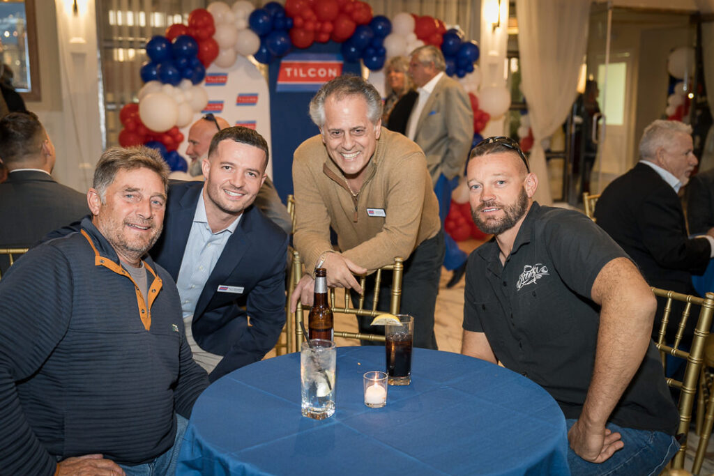 Four men seated at table during Tilcon corporate appreciation event with blue tablecloth