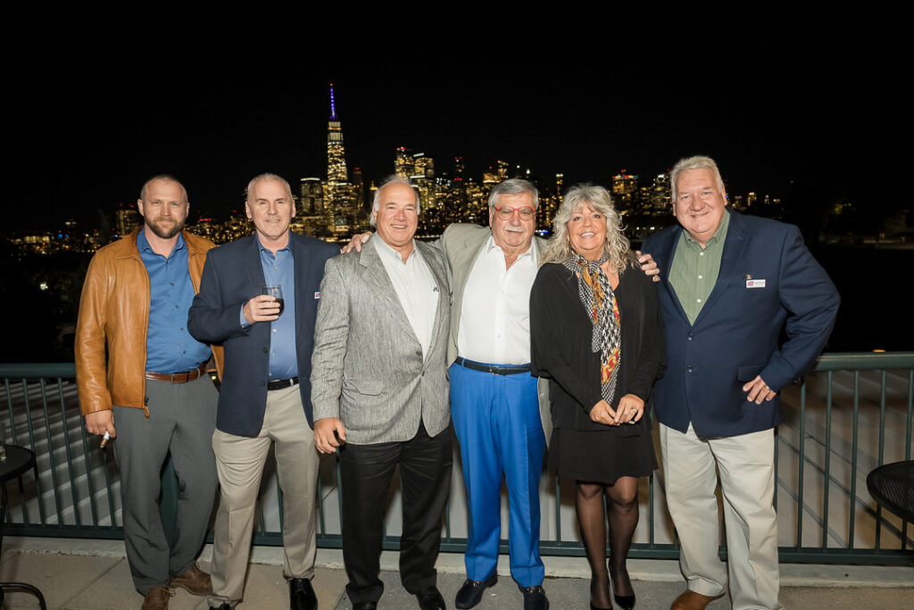Six guests posing on terrace with illuminated New York City skyline at night