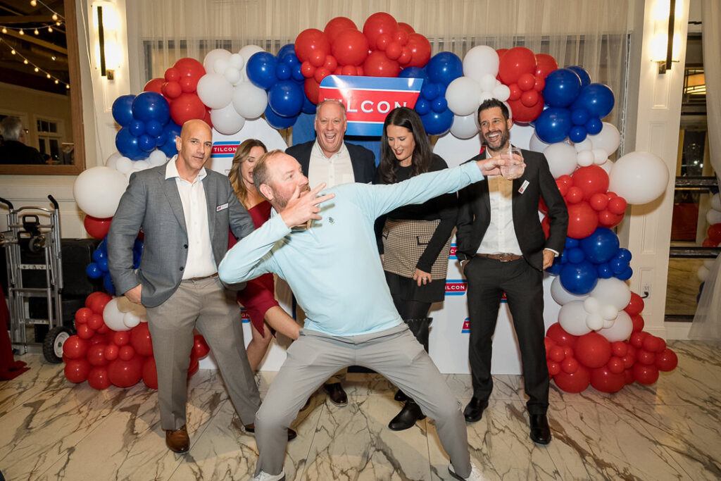 Group of guests striking playful poses in front of Tilcon balloon backdrop with red white and blue colors