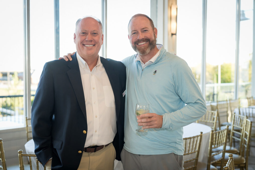 Two executives smiling at Tilcon New York client appreciation event with windows behind