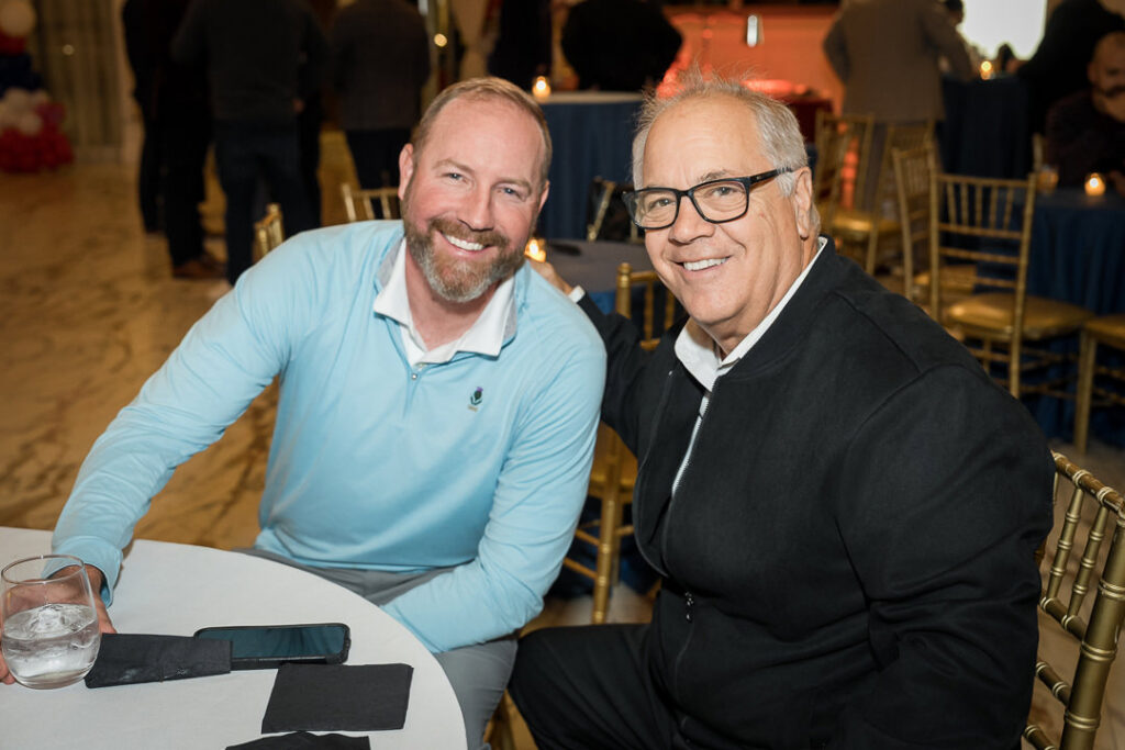Two men smiling at table during Tilcon evening event with warm lighting