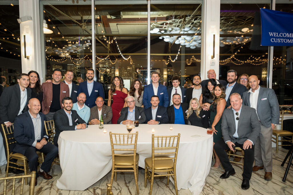 Large group photo of Tilcon team and guests at client appreciation day with NYC skyline visible through windows