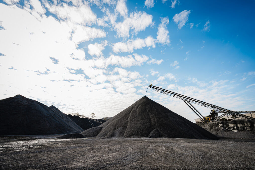 Dramatic view of large aggregate mounds under dynamic clouded sky at Clinton Point Quarry industrial site.