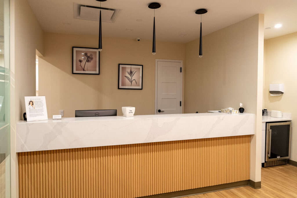 Close-up of Canopy Dental reception desk with white marble countertop, vertical wood slats, and modern pendant lighting, dental office photography by Alex Kaplan