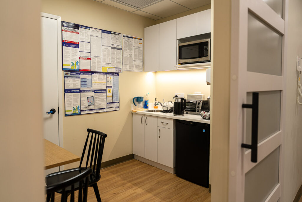 Staff kitchenette with built-in microwave, white cabinets, under-cabinet lighting, and modern black appliances, Alex Kaplan commercial photography NYC