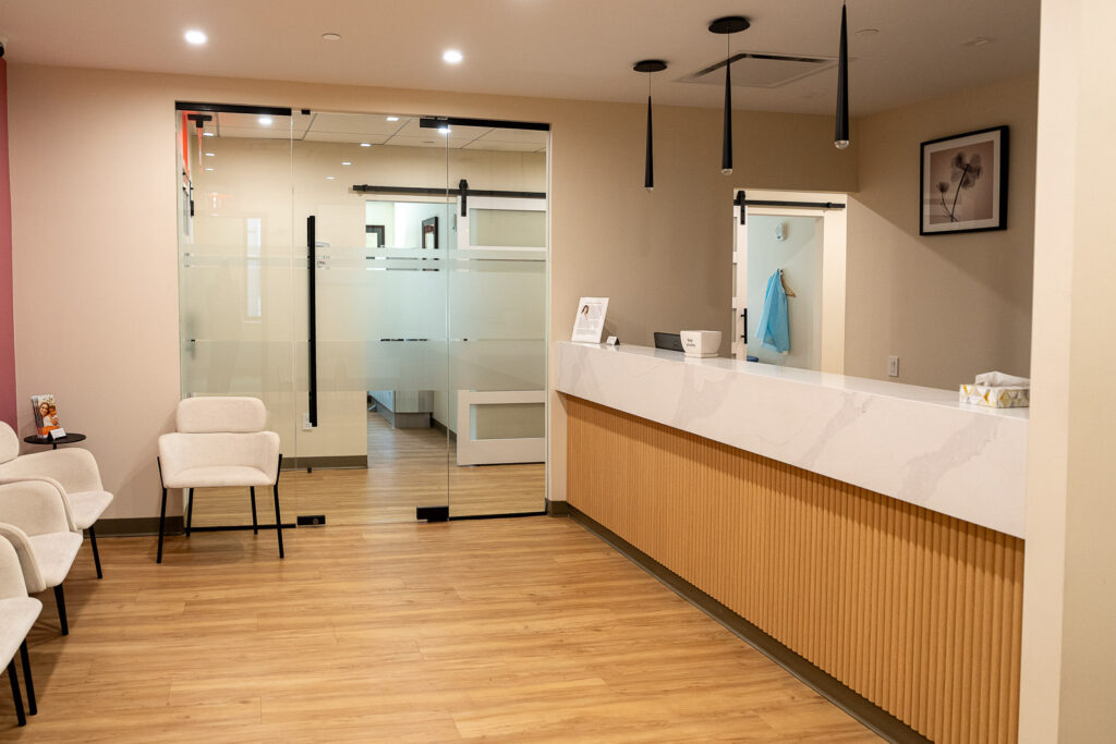 Modern dental practice reception area viewed through frameless glass sliding doors with black hardware, professional healthcare photography by Alex Kaplan