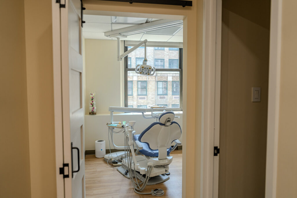Treatment room viewed through modern doorway with sliding barn door showing dental chair and natural window light, dental practice photography by Alex Kaplan