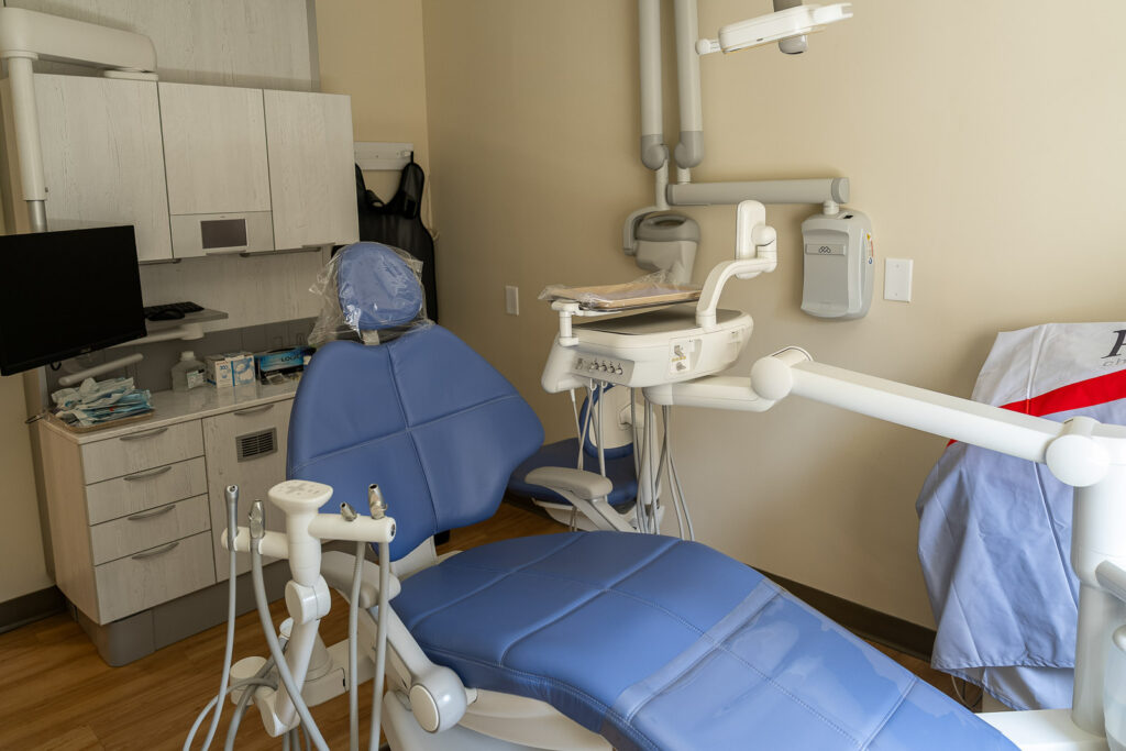 Professional dental treatment room with blue upholstered chair, light wood cabinetry, and advanced imaging equipment, Alex Kaplan dental office photography