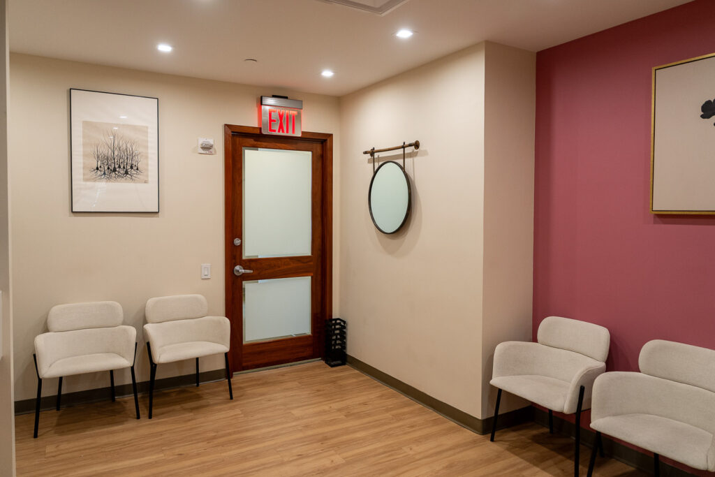 Modern dental waiting area featuring cream seating, contemporary art, and wood door with frosted glass, professional practice photography by Alex Kaplan