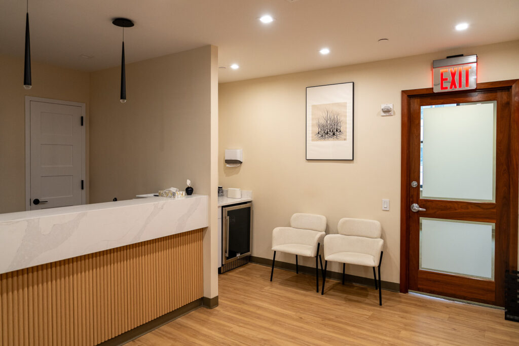 Comfortable waiting room with modern cream upholstered chairs, warm wood exit door, and botanical artwork at Canopy Dentistry NYC, Alex Kaplan Photography