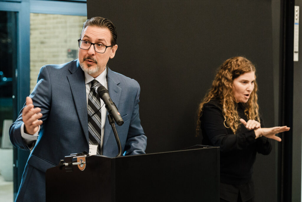 Clergy member and ASL interpreter addressing attendees during HKNC Walters-Smithdas Atrium dedication