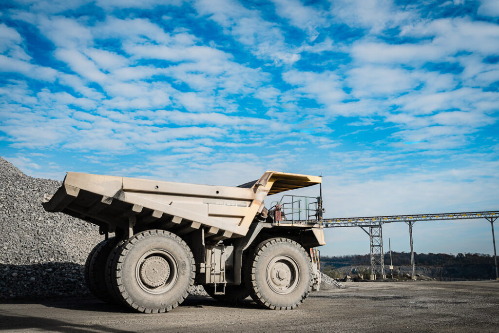 Large articulated haul truck moving through quarry yard surrounded by stone stockpiles and processing equipment.