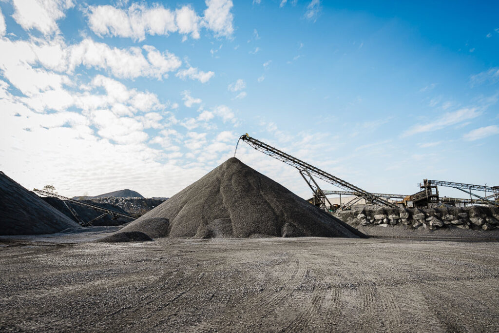 Dark aggregate stockpiles with conveyor system running overhead at Clinton Point Quarry in New Hamburg, New York.
