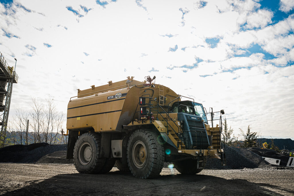 Articulated dump truck traveling along quarry road with conveyor system visible in background at Clinton Point.
