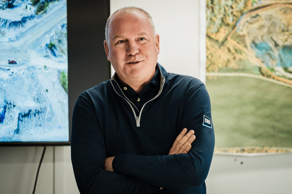 Professional portrait of Tilcon executive in navy pullover with arms crossed and quarry imagery in background