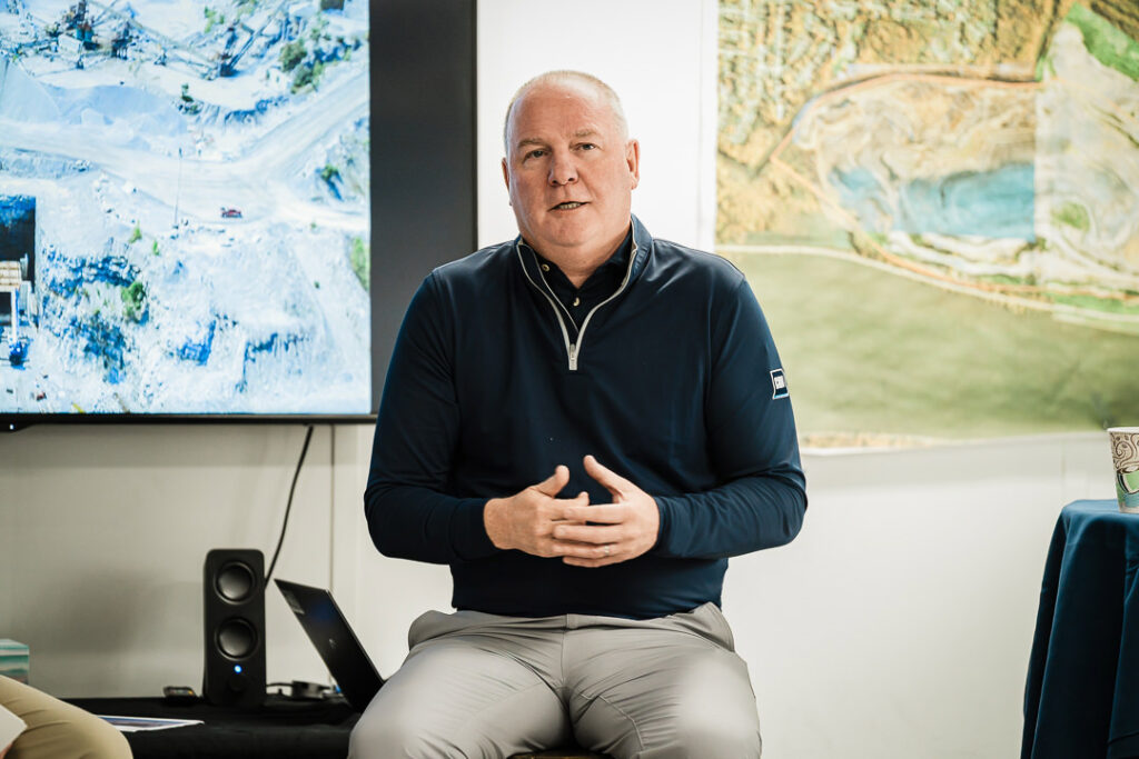 Professional portrait of Tilcon CEO in navy pullover with quarry imagery on screen in background