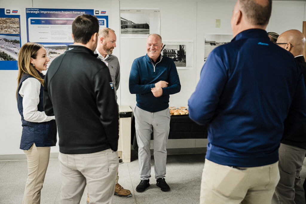 Group of Tilcon team members gathered for strategic planning discussion with project forecast board visible in background
