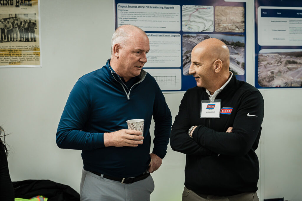 Two Tilcon executives in business casual having friendly conversation with project boards visible behind them