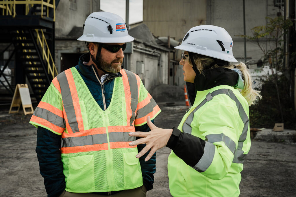 Two Tilcon executives in safety gear having conversation at Clinton Point Quarry with industrial facility in background