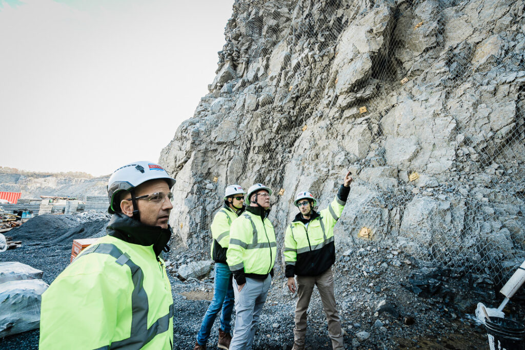 Tilcon executives in safety gear looking up at towering quarry rock face with geological layers visible
