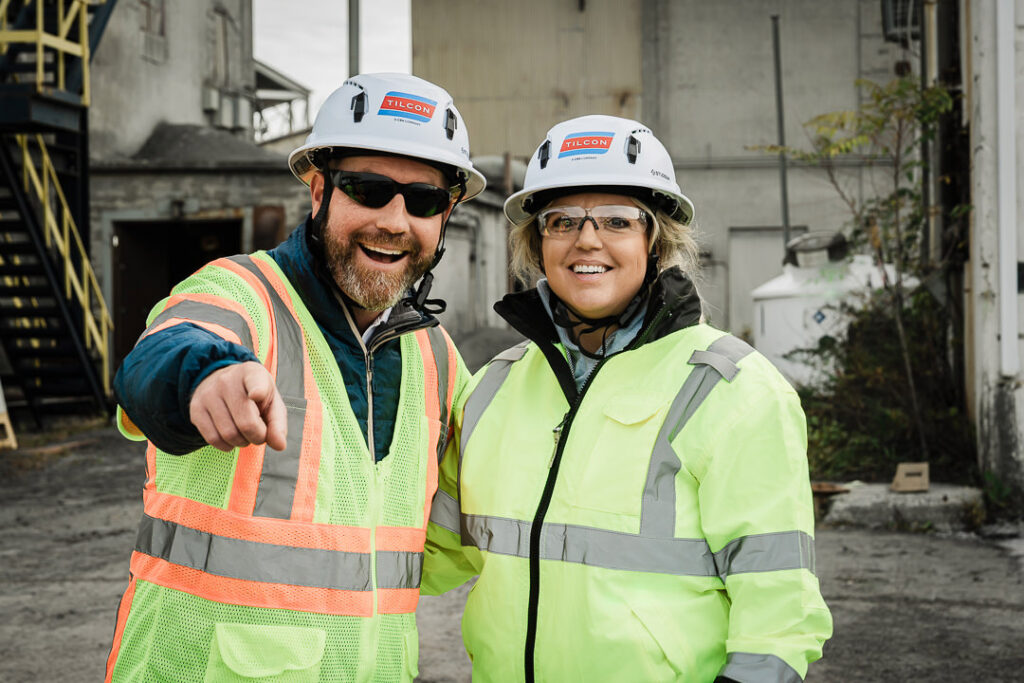Male and female Tilcon executives in hard hats and safety vests with one pointing during site tour discussion