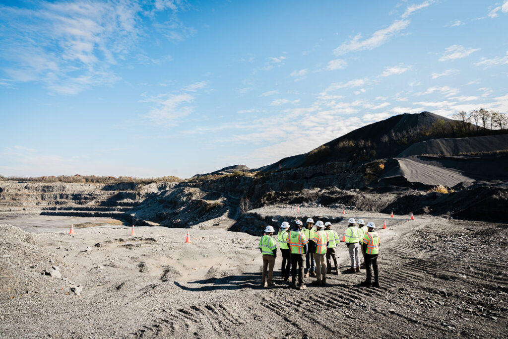 Wide shot of Tilcon team gathered on quarry floor with terraced pit walls and operations visible in background