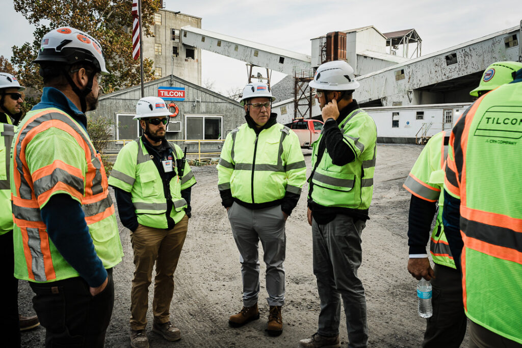 Group of Tilcon team members in safety gear gathered outside quarry office building with Tilcon signage and American flag