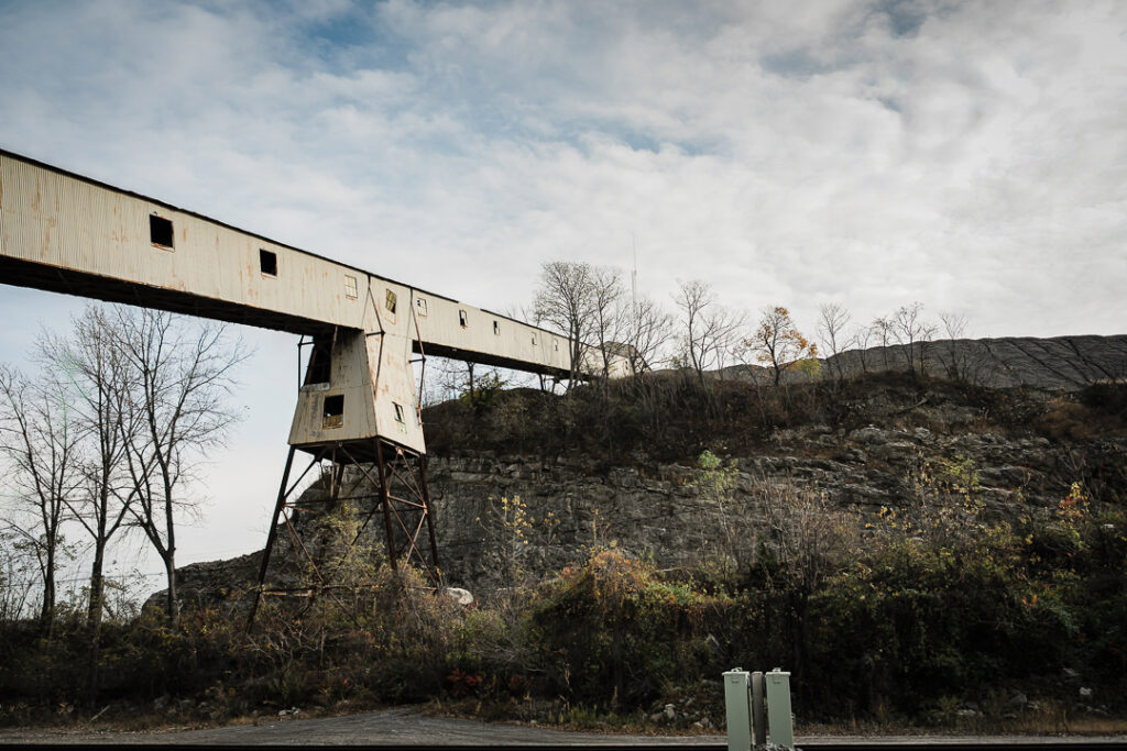 Large concrete processing tower with conveyor belt system at Clinton Point Quarry with hillside in background