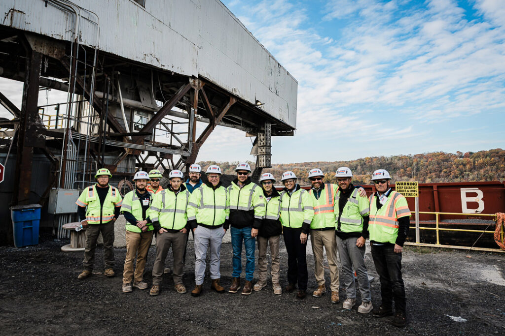Large group of Tilcon employees in safety gear standing beneath massive quarry conveyor system for group photo