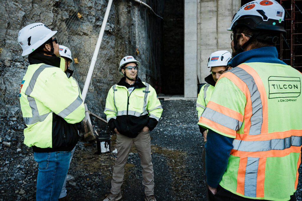 Small group of Tilcon executives in safety gear discussing operations near quarry processing facility