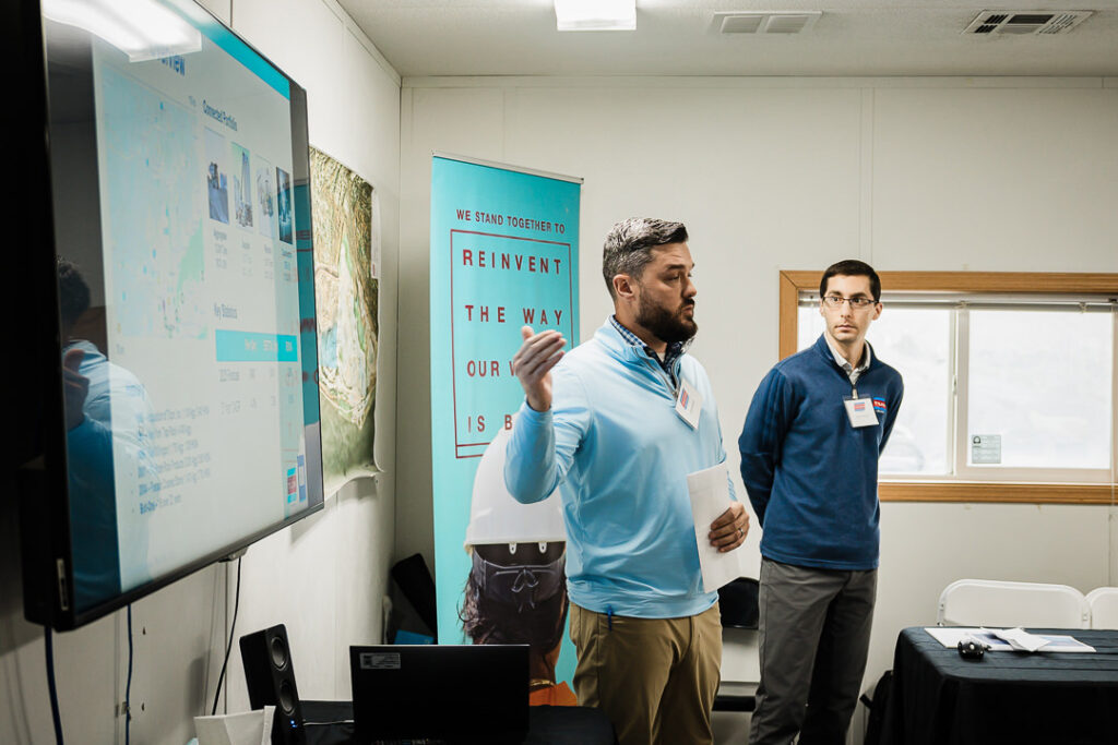 Team member in safety vest presents to executives beside 'We Stand Together' banner