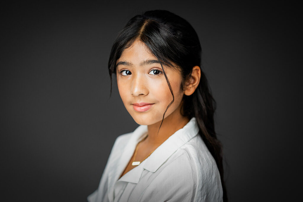 Commercial actor headshot with clean gray background and white blazer showing versatility and approachability for casting directors