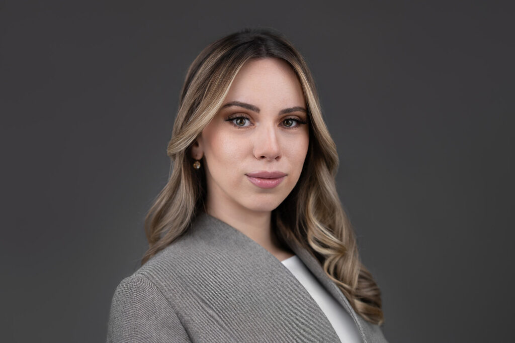Corporate headshot of Ana Tasevska wearing a gray blazer against a dark charcoal studio background