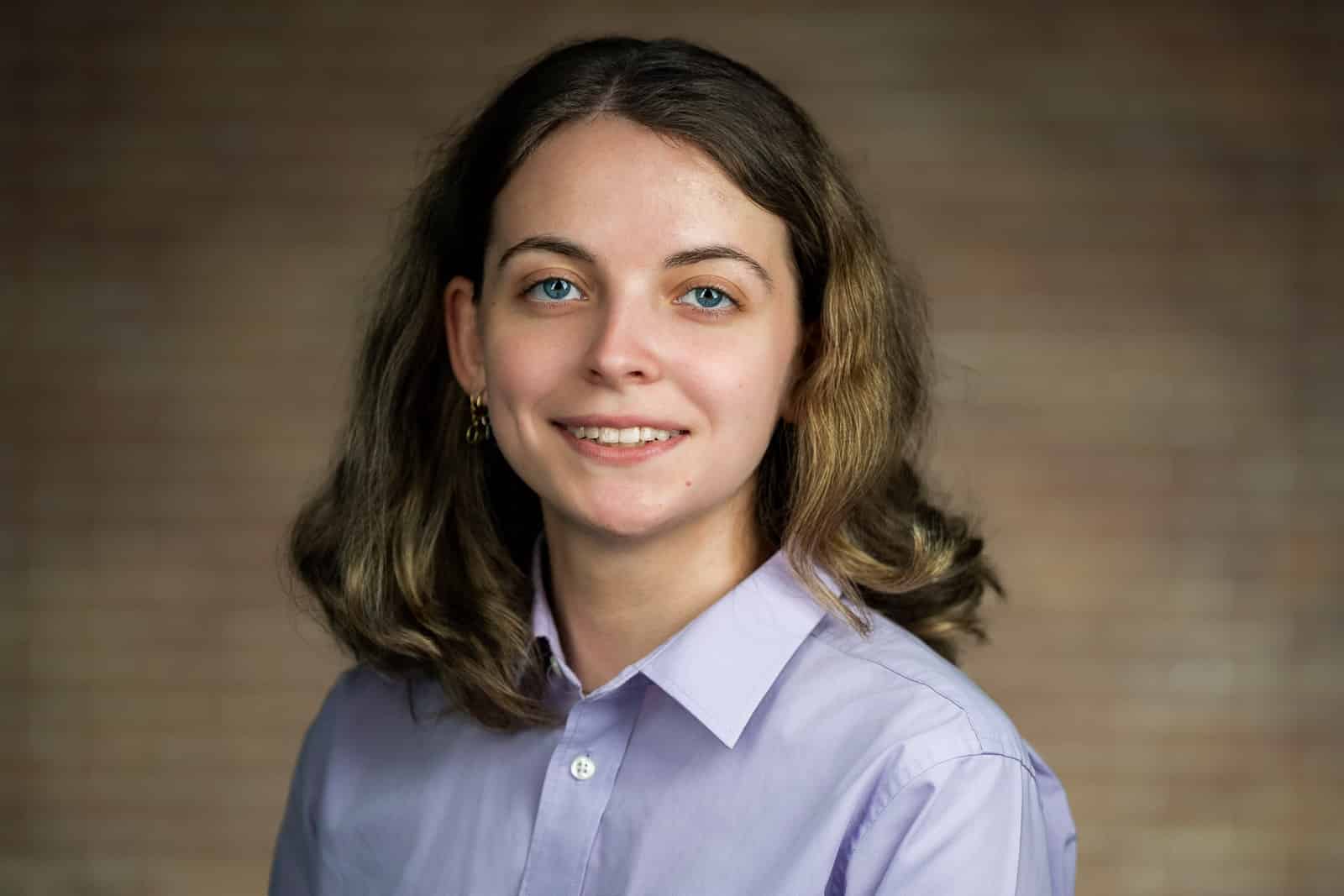 Corporate team headshot of young woman in lavender shirt warm wood background NJ