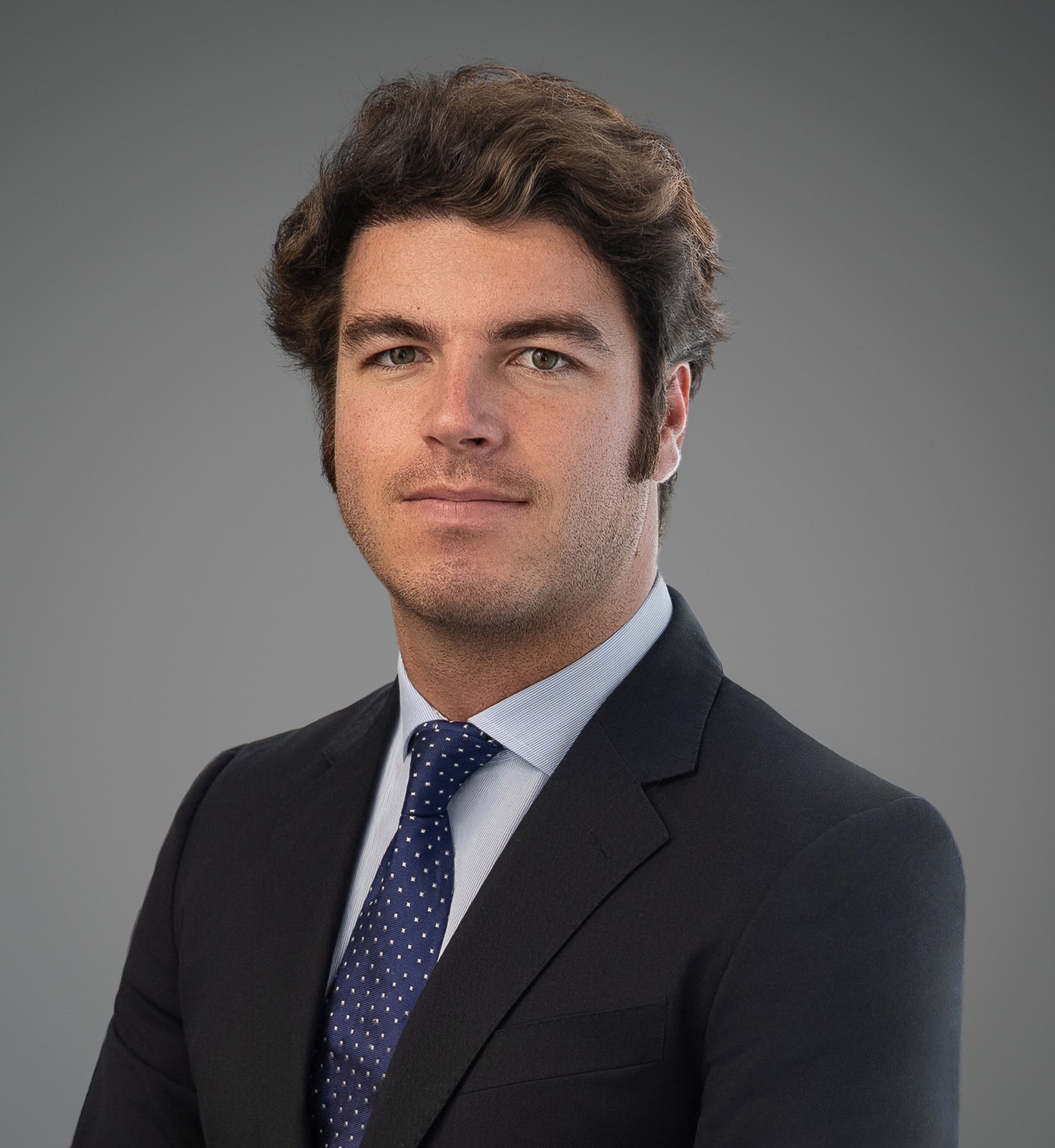 Ignacio Alonso wearing a dark suit and blue tie in a professional gray-background headshot