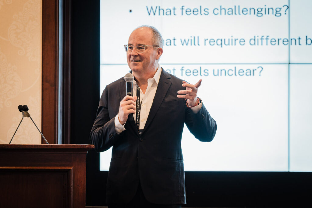 Corporate leader addressing an audience from stage with a presentation slide visible at a New Jersey business event