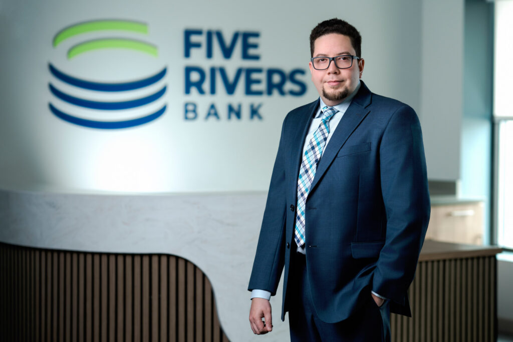 Corporate headshot of man in blue suit with glasses and plaid checked tie