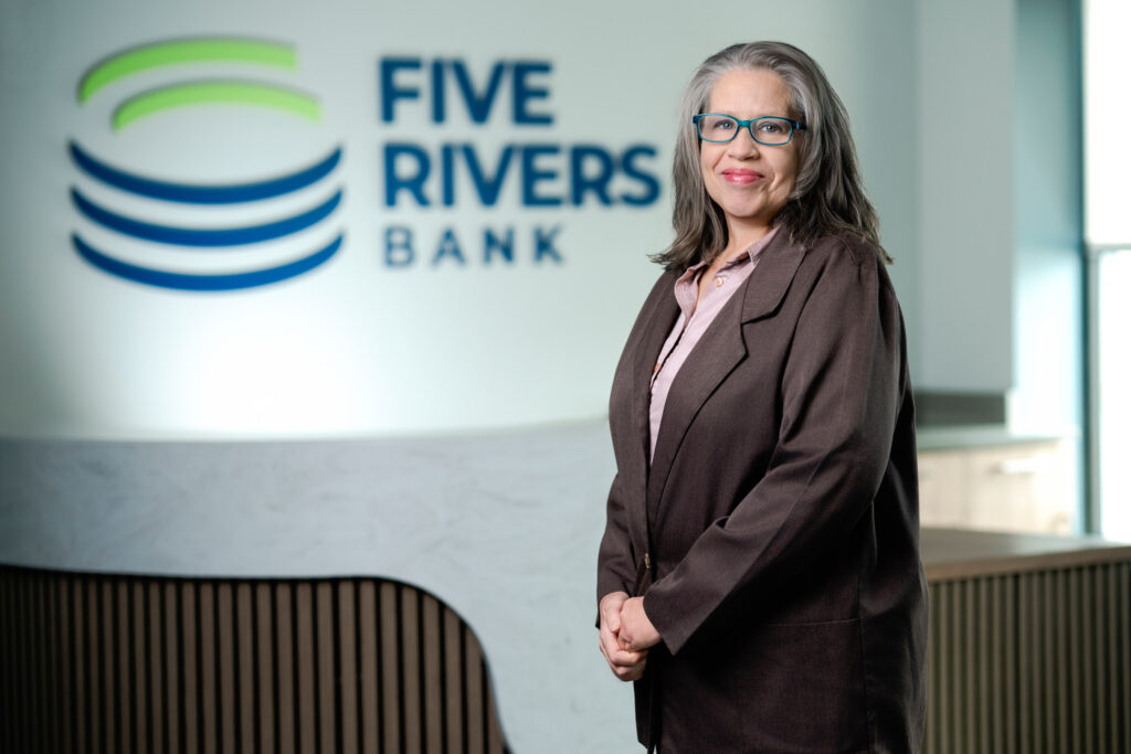 Professional headshot of woman with glasses in brown blazer and light pink blouse