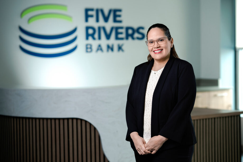 Corporate headshot of woman with glasses in black blazer and white patterned top