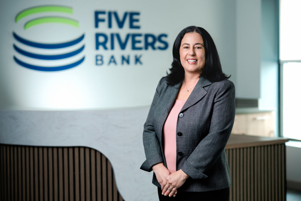 Professional headshot of woman in gray blazer and pink top smiling confidently