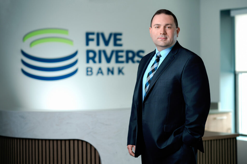 Corporate headshot of man in navy suit and striped tie with Five Rivers Bank backdrop
