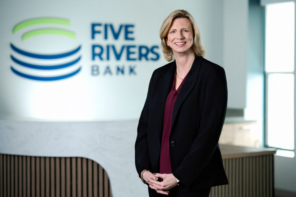 Friendly corporate headshot of woman in black blazer and burgundy top smiling warmly