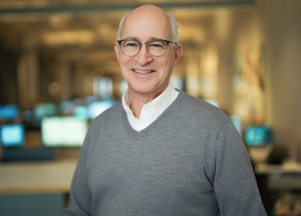 Corporate team headshot of a senior professional in a gray sweater and glasses photographed at a New York City company office Caption (optional): NYC corporate headshot photographer — consistent team results