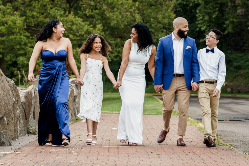 Family of five in coordinated blue and white outfits walking hand in hand along brick pathway at Ross Dock Picnic Area in Fort Lee New Jersey