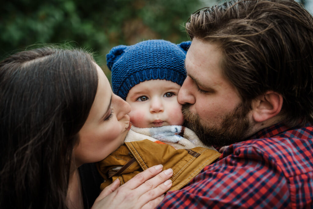 Parents kissing their baby on both cheeks during an authentic outdoor family portrait session at Knight Park in New Jersey