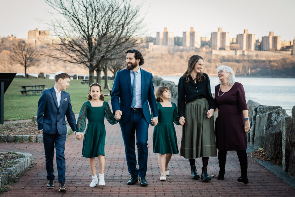 Family walking together in coordinated neutral and jewel-tone outfits during a golden hour session along the Hudson River in New Jersey