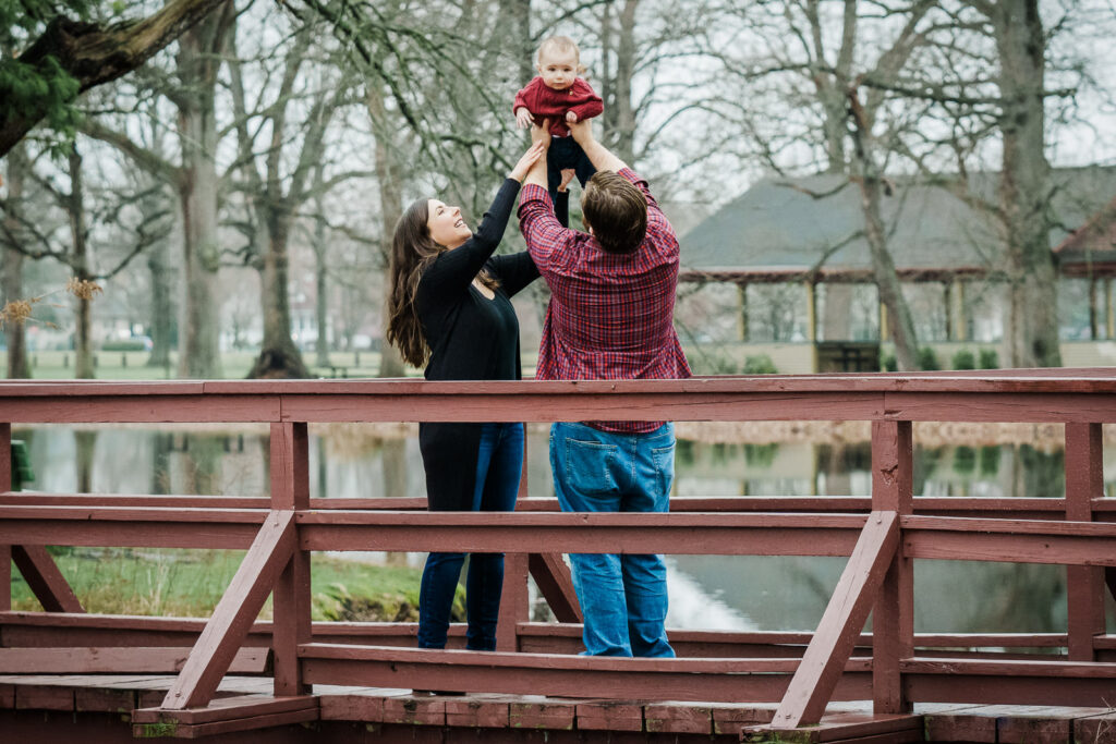 683.jpg Filename: kids-family-photoshoot-relaxed-moment-northern-nj.jpg Alt text: Father lifting baby while mother laughs during a relaxed outdoor family photoshoot at Knight Park in Collingswood New Jersey
