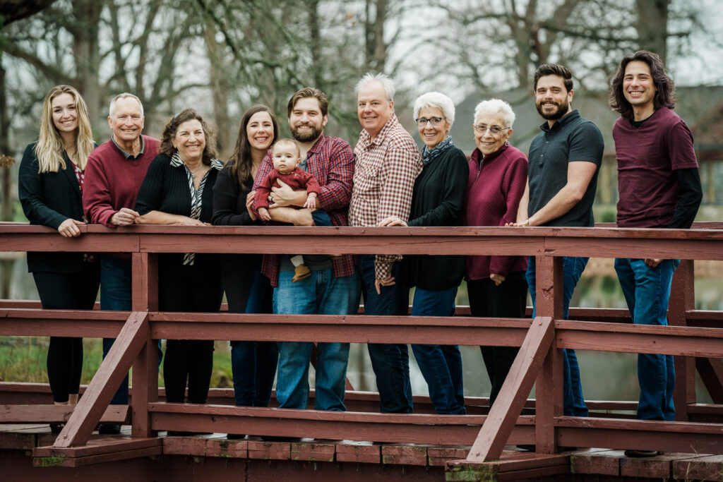 Extended multi-generational family of ten posing together on red wooden bridge at Knight Park in Collingswood New Jersey