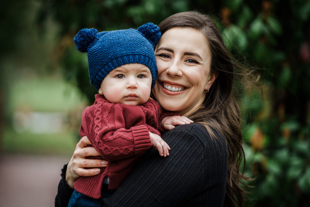 Mother holding baby boy in blue knit hat during outdoor family portrait session at Knight Park in Collingswood New Jersey