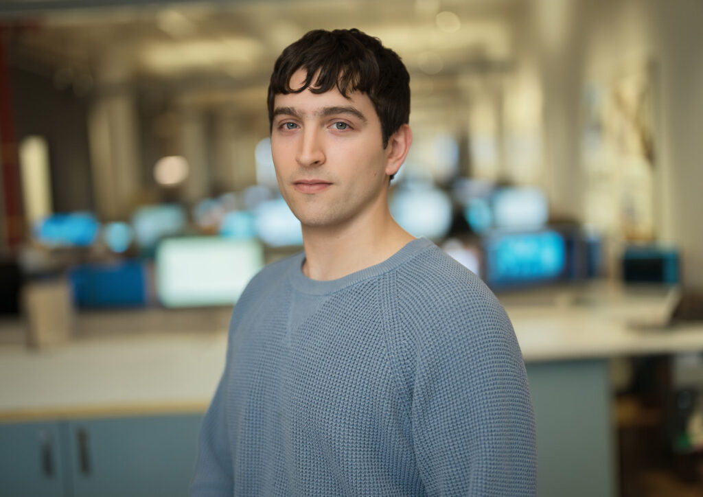 Professional team headshot of a young man in a blue sweater photographed at a New York City technology company office Caption (optional): Professional team headshots NYC — on-site office session